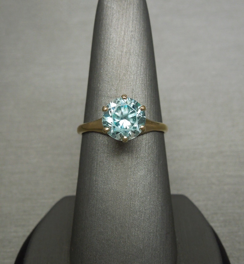 May include: A gold ring with a large, round, light blue gemstone set in a prong setting.