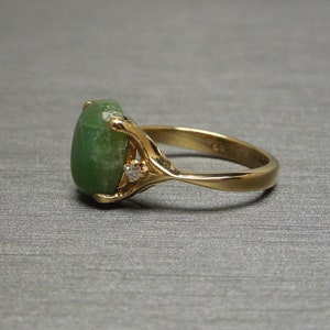 K&ouml;nnte beinhalten: Ein goldener Ring mit einem gr&uuml;nen ovalen Edelstein und zwei kleinen Diamanten auf der Ringschiene.