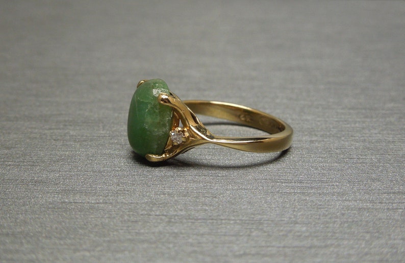 K&ouml;nnte beinhalten: Ein goldener Ring mit einem gr&uuml;nen ovalen Edelstein und zwei kleinen Diamanten auf der Ringschiene.