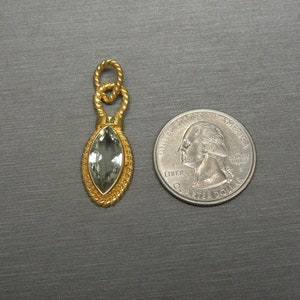 May include: A gold pendant featuring a green gemstone in a marquise shape. The pendant is displayed against a grey background.