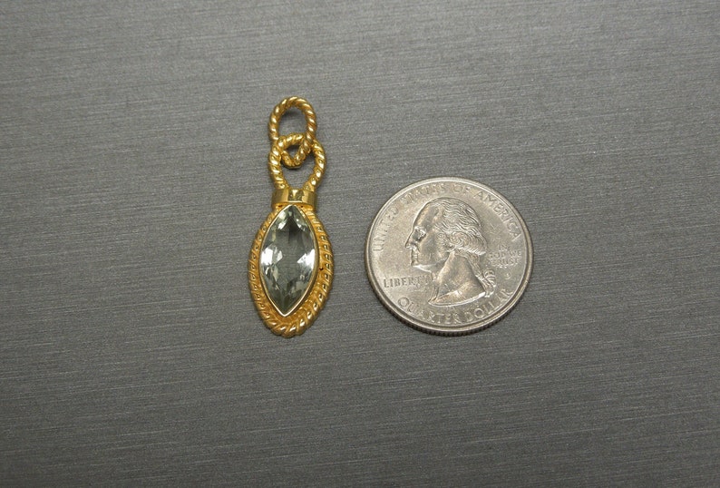 May include: A gold pendant featuring a green gemstone in a marquise shape. The pendant is displayed against a grey background.