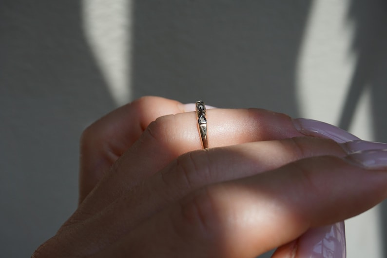 May include: A gold ring featuring a repeating design of small, clear stones. The ring is worn on a finger, with sunlight creating shadows. The ring's intricate details are highlighted. The ring is a piece of jewellery.