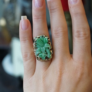 May include: A green jade ring with a carved flower design set in a gold filigree setting.