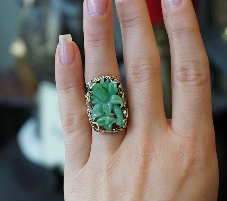 May include: A green jade ring with a carved flower design set in a gold filigree setting.