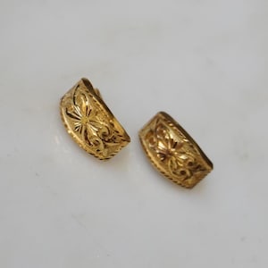 May include: A pair of gold-toned earrings with a floral design. The earrings are made of metal and have a curved shape.