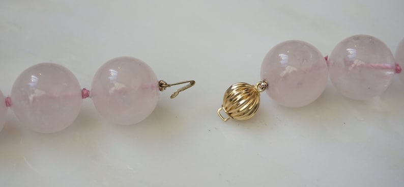 May include: A pink rose quartz beaded necklace with a gold clasp. The beads are large and round.