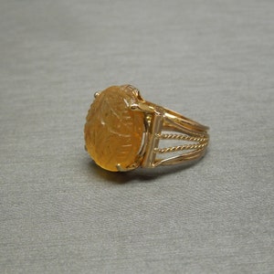Op de afbeelding: Een gouden ring met een gegraveerde barnsteen. De steen is ovaalvormig en heeft een gedetailleerd ontwerp.