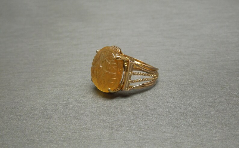 Op de afbeelding: Een gouden ring met een gegraveerde barnsteen. De steen is ovaalvormig en heeft een gedetailleerd ontwerp.