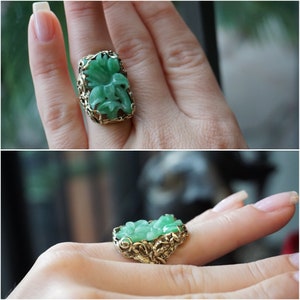 May include: A green jade ring with a floral design set in gold. The ring is on a finger.