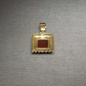 May include: Gold pendant with a square red gemstone set in a gold frame.