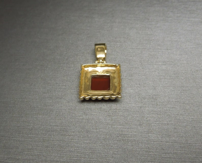 May include: Gold pendant with a square red gemstone set in a gold frame.