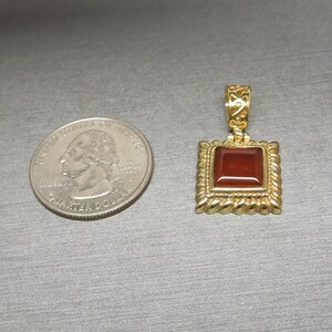 May include: A gold pendant with a square red carnelian gemstone set in a gold frame. The pendant is about the size of a US quarter.