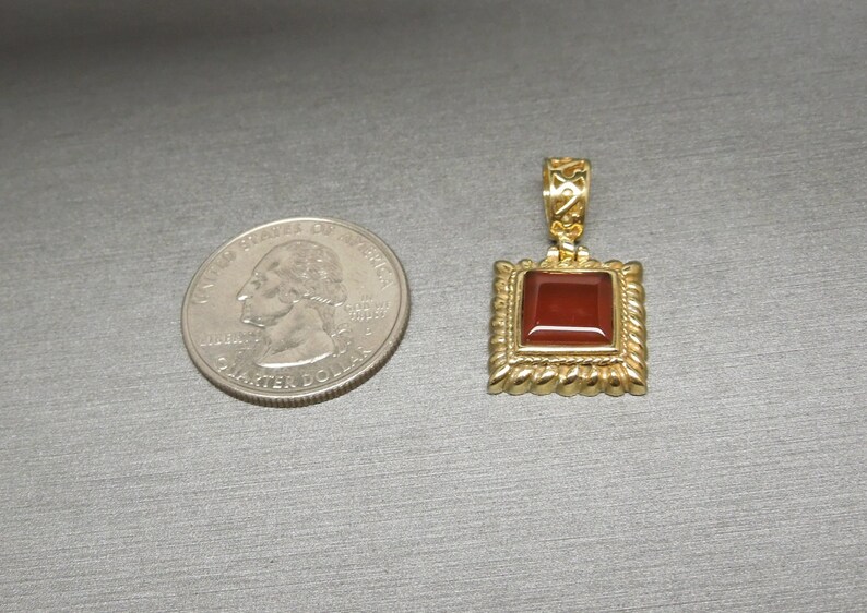 May include: A gold pendant with a square red carnelian gemstone set in a gold frame. The pendant is about the size of a US quarter.