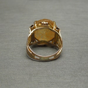 Op de afbeelding: Een gouden ring met een grote, ovale, gele edelsteen gezet in een filigraan ontwerp.