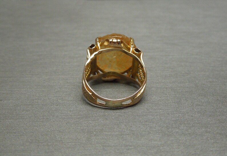 Op de afbeelding: Een gouden ring met een grote, ovale, gele edelsteen gezet in een filigraan ontwerp.