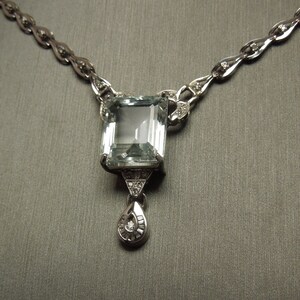 K&ouml;nnte beinhalten: Elegante Silberkette mit einem gro&szlig;en, rechteckigen, hellblauen Edelsteinanh&auml;nger. Der Anh&auml;nger ist mit kleineren Diamanten und einem tropfenf&ouml;rmigen Anh&auml;nger verziert. Die Kette hat ein filigranes Design mit kleinen Diamantakzenten.