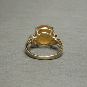 May include: A gold ring with a large oval-shaped orange gemstone set in a prong setting. The ring has a delicate, intricate design.