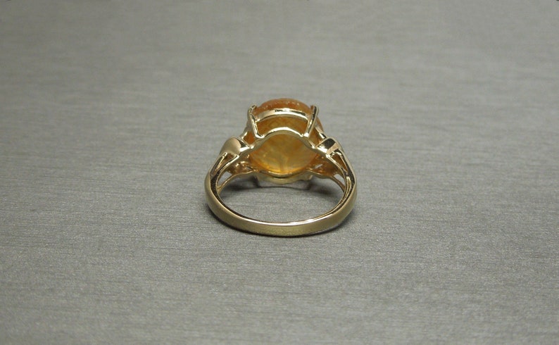 May include: A gold ring with a large oval-shaped orange gemstone set in a prong setting. The ring has a delicate, intricate design.