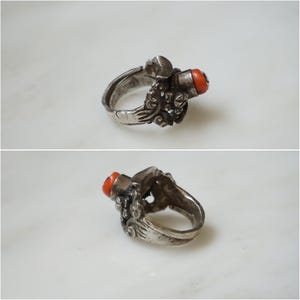 May include: A silver ring with an intricate design and a red coral stone. The ring is set on a white background.