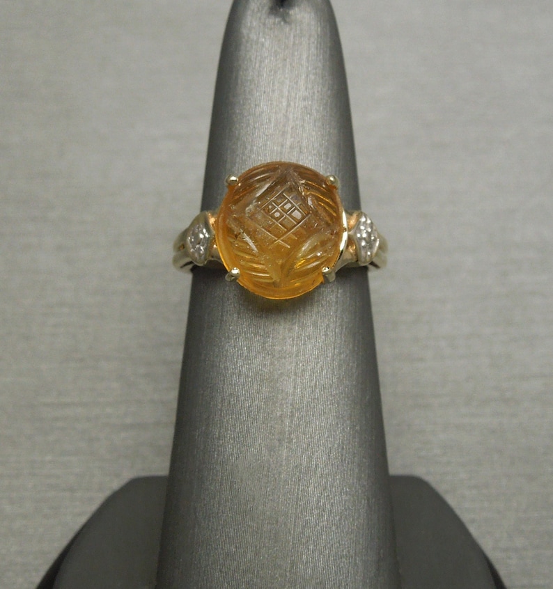 May include: A gold ring with a carved orange gemstone and two small diamonds on the sides.