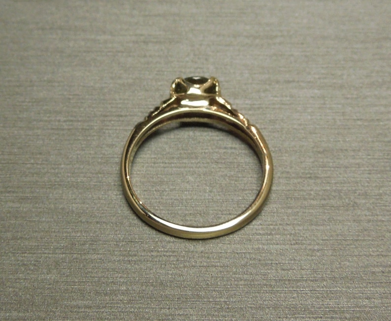 May include: A gold ring with a single, round, dark gemstone set in a prong setting. The ring has a delicate, ornate band.