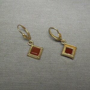 May include: A pair of gold earrings with a square red gemstone in the center of each earring.