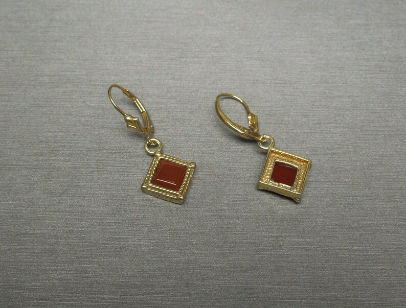 May include: A pair of gold earrings with a square red gemstone in the center of each earring.