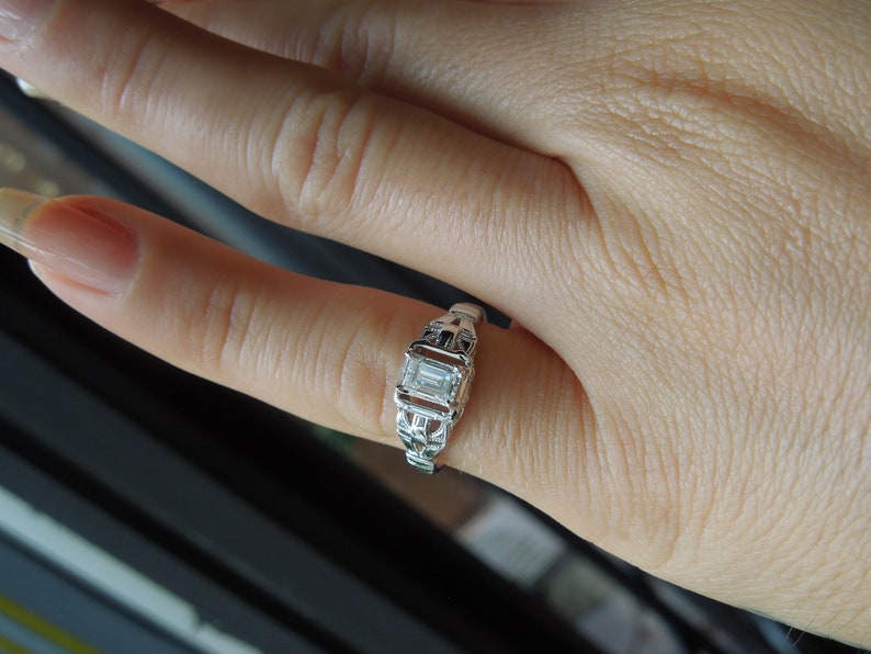 May include: A silver ring with a clear, rectangular-shaped gemstone set in a delicate, intricate design.