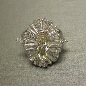 Op de afbeelding: Een ring van witgoud met een gele marquise-diamant, omgeven door een halo van kleinere diamanten.