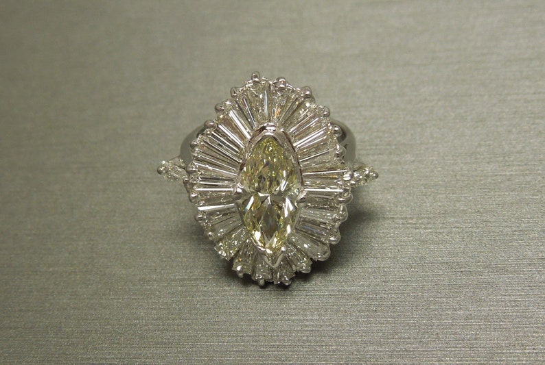 Op de afbeelding: Een ring van witgoud met een gele marquise-diamant, omgeven door een halo van kleinere diamanten.