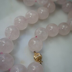 May include: A pink rose quartz beaded necklace with a gold clasp. The beads are large and round, and the necklace is strung on a pink thread.