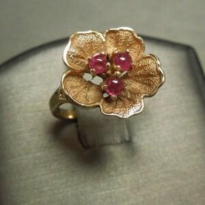 May include: A gold ring with a flower design featuring three pink gemstones.