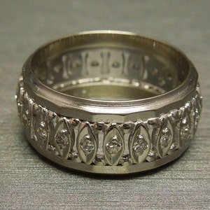 May include: A silver wedding band with a decorative design featuring small diamonds set in a repeating pattern.