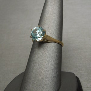 May include: A gold ring with a large, round, light blue gemstone set in a prong setting.