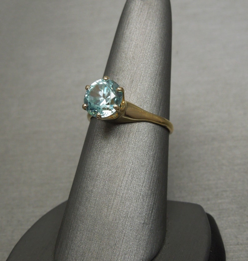May include: A gold ring with a large, round, light blue gemstone set in a prong setting.