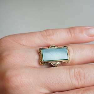 May include: A gold ring with a green stone set in a rectangular frame.