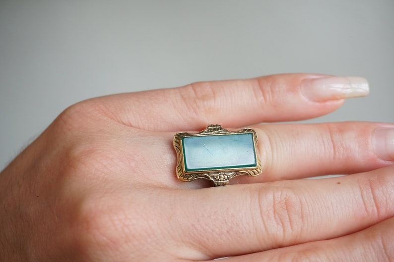 May include: A gold ring with a green stone set in a rectangular frame.