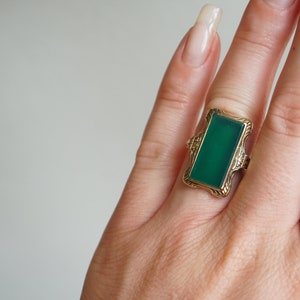 May include: A gold ring with a green rectangular gemstone set in a decorative frame.