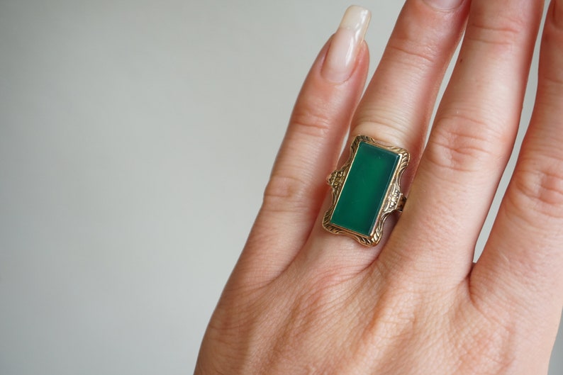 May include: A gold ring with a green rectangular gemstone set in a decorative frame.