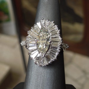 Op de afbeelding: Een ring met een marquise-geslepen diamant met een halo van baguette-geslepen diamanten. De ring is gezet in witgoud en heeft een delicate band.