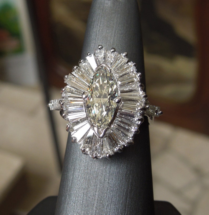 Op de afbeelding: Een ring met een marquise-geslepen diamant met een halo van baguette-geslepen diamanten. De ring is gezet in witgoud en heeft een delicate band.