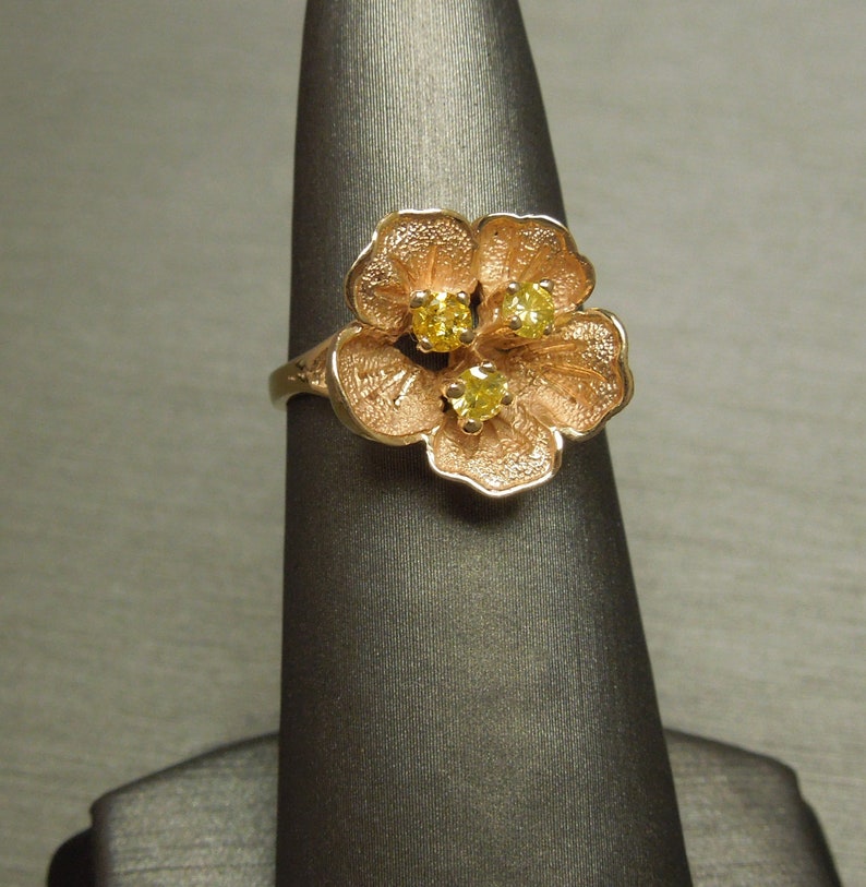 May include: A gold ring with a flower design featuring three yellow gemstones.