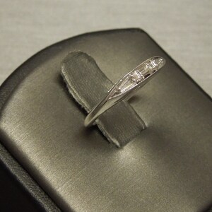 May include: A silver band ring with five small, clear baguette-cut diamonds set in a row.