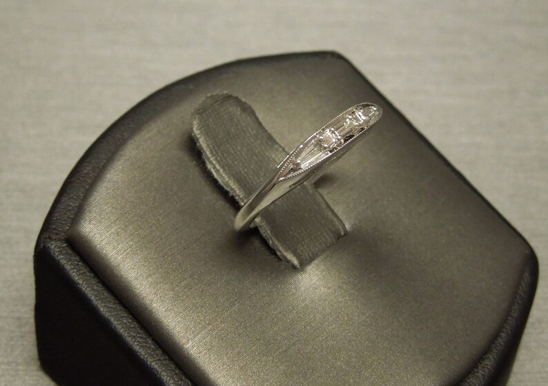 May include: A silver band ring with five small, clear baguette-cut diamonds set in a row.
