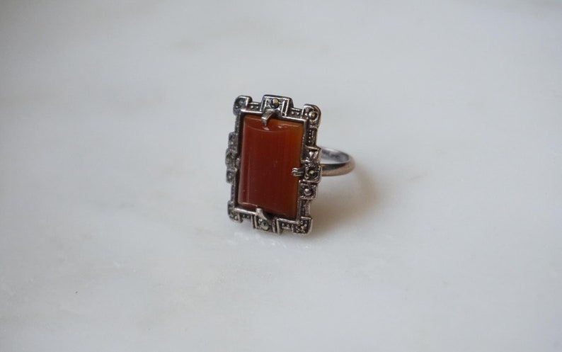 May include: A silver ring with a rectangular carnelian stone set in a geometric frame of marcasite.
