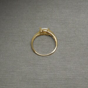 K&ouml;nnte beinhalten: Ein goldener Ring mit einem wei&szlig;en ovalen Edelstein, der in einer Krappenfassung sitzt.