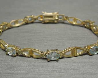 May include: A gold bracelet with a delicate design featuring oval-shaped aquamarine gemstones. The bracelet has a clasp closure.
