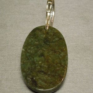 May include: A green oval pendant with a silver bail. The pendant is made of a natural stone with a mottled pattern.