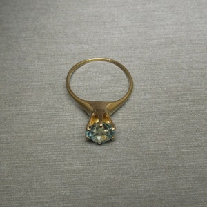 May include: A gold ring with a blue gemstone set in a prong setting.