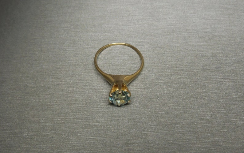 May include: A gold ring with a blue gemstone set in a prong setting.